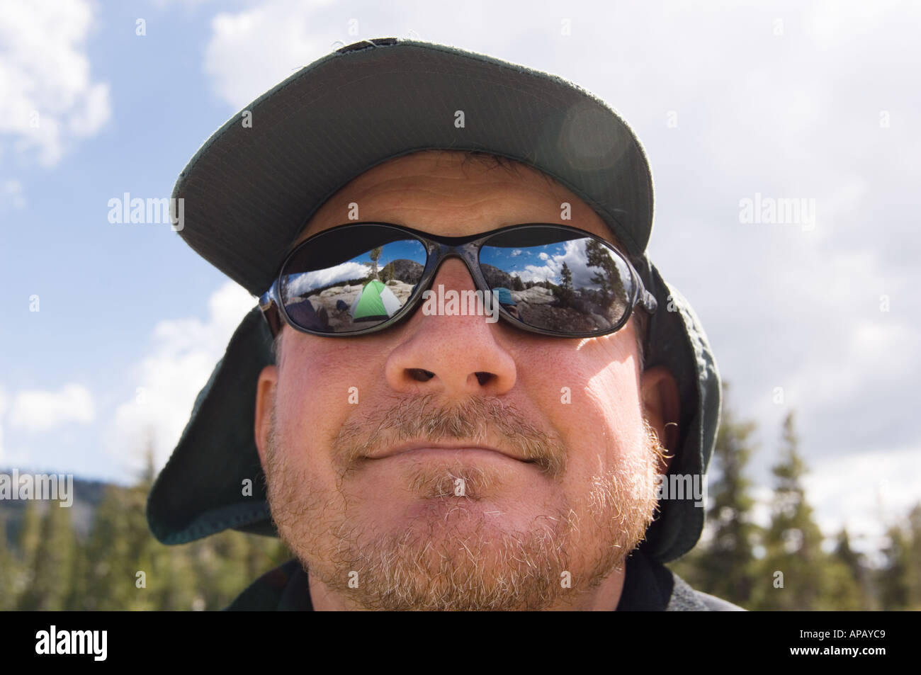 Color horizontal image of the face of a middle aged man in a hiking cap and sunglasses reflecting a tent with a goatee in front Stock Photo