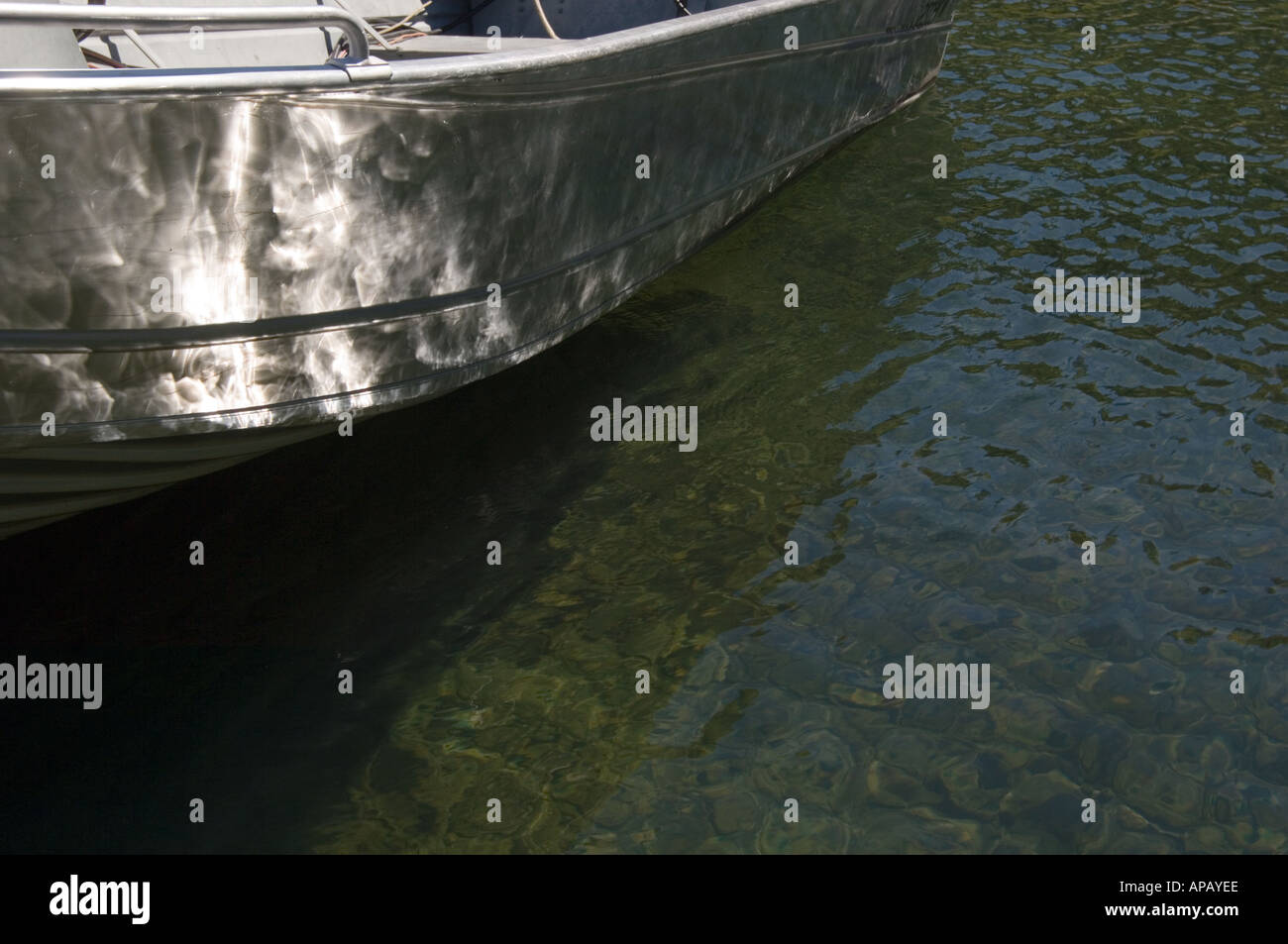 waterline of an aluminum skiff on a lake with small waves with sunlight reflecting from between lake and keel refracting Stock Photo