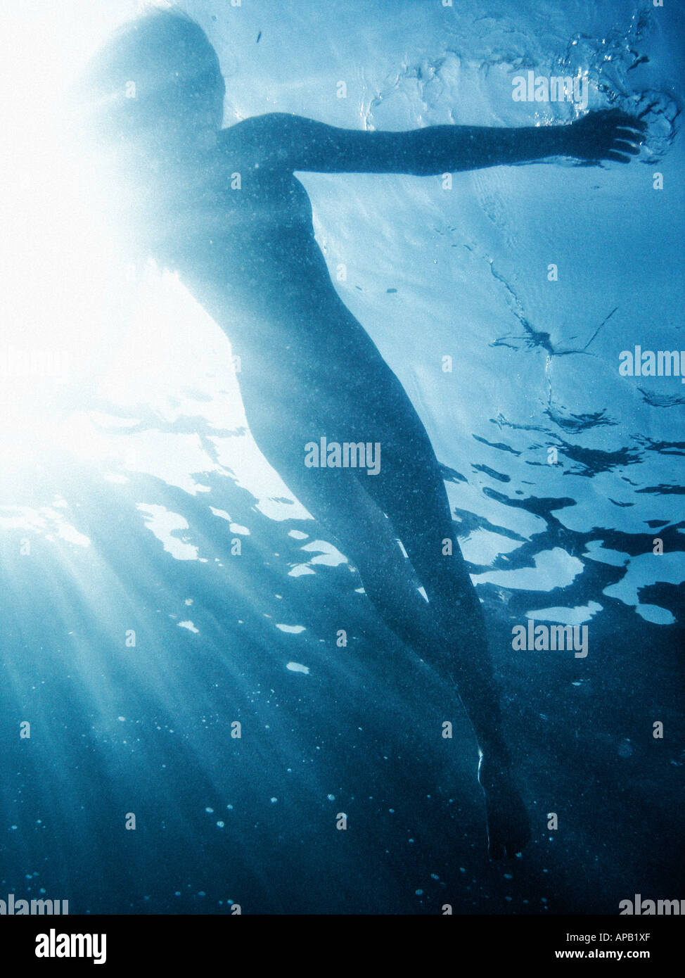 Girl free diving with a shaft of sunlight behind her Stock Photo