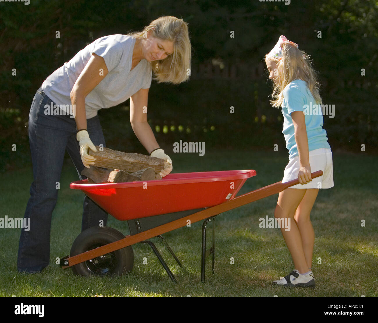 Mother and daughter putting firewood in a wheelbarrow Stock Photo - Alamy