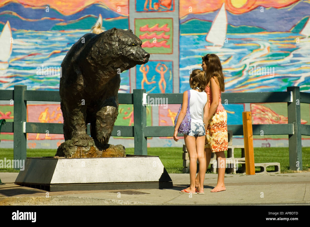 IDAHO COEUR D ALENE COLORFUL DOWNTOWN SCENE GIRLS LOOKING AT GRIZZLY BEAR STATUE Stock Photo