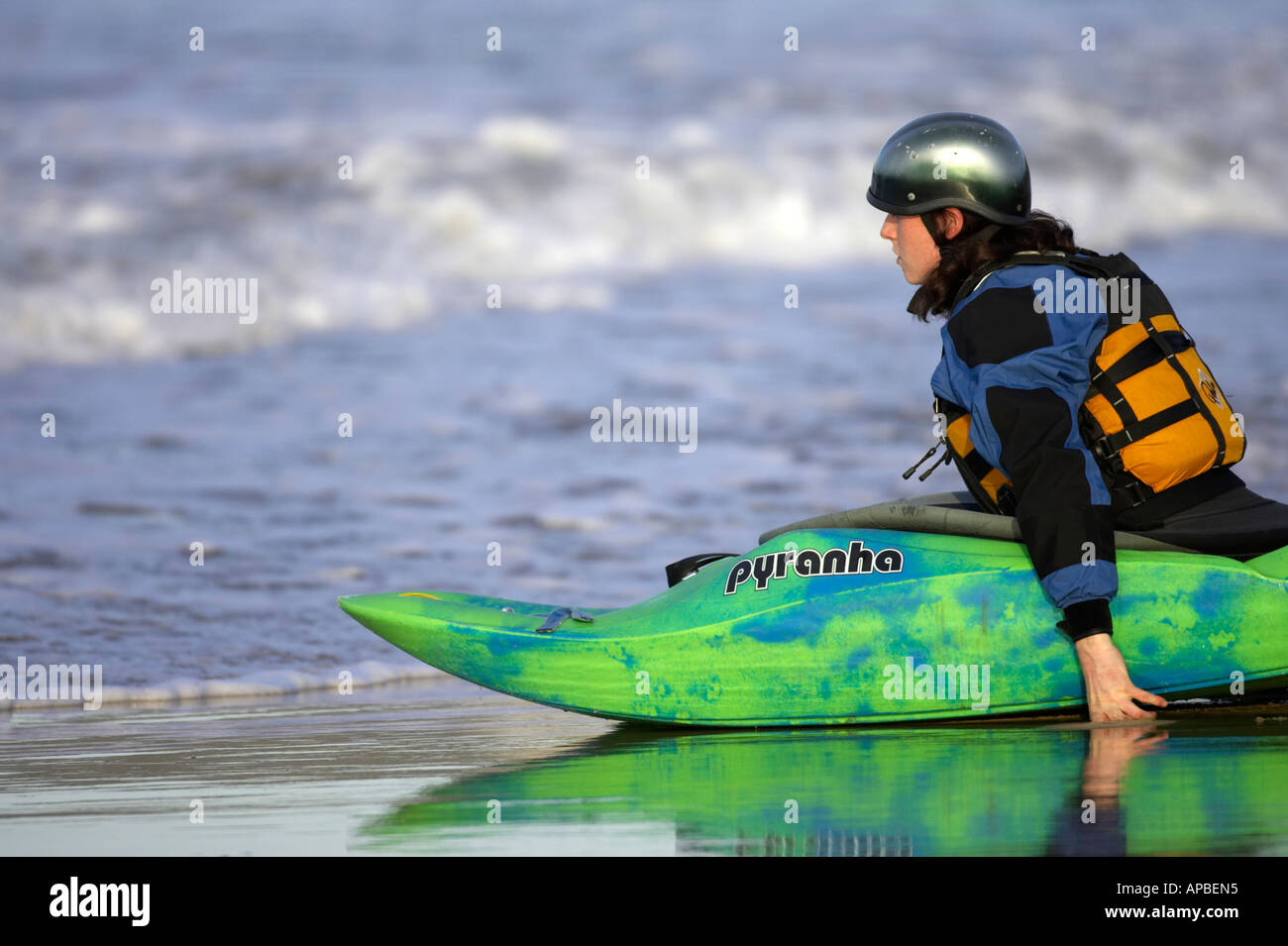 female kayaker pushes her sea kayak off the beach into the water from