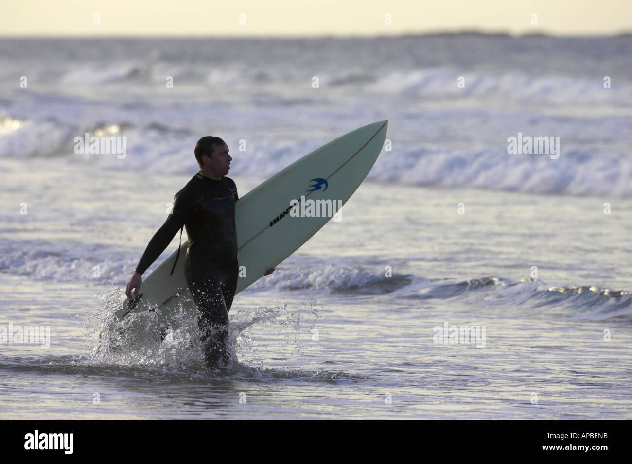man in wetsuit carrying surfboard into the sea off white rocks beach