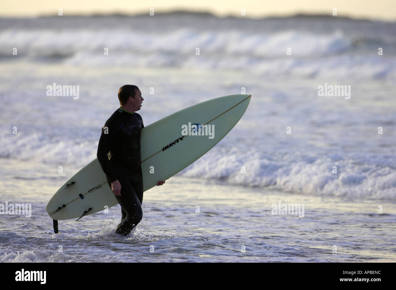 man in wetsuit carrying surfboard into the sea off white rocks beach portrush county antrim