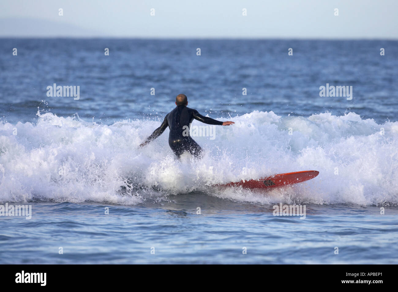 male surfer in wetsuit on red surfboard surfs through wave off white rocks beach portrush county