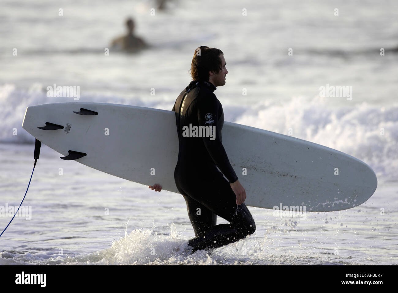 man in wet suit carrying surf board into the sea on white rocks beach