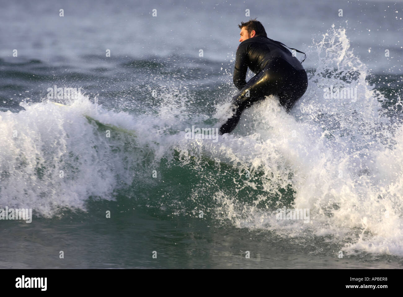 male surfer in wetsuit surfs through wave off white rocks beach