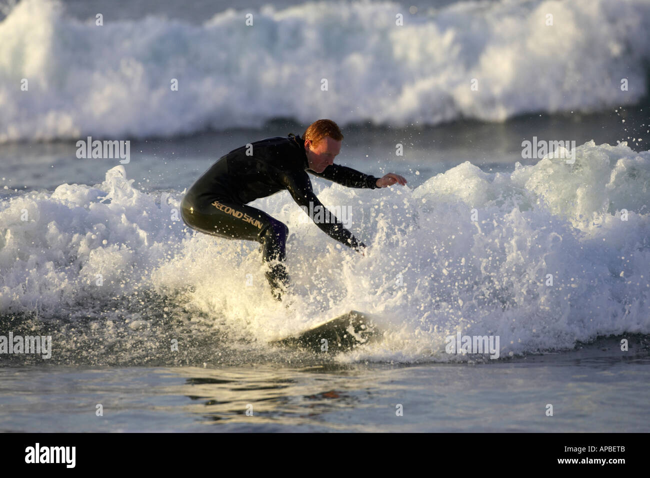 male surfer in wetsuit surfs on waves off white rocks beach portrush