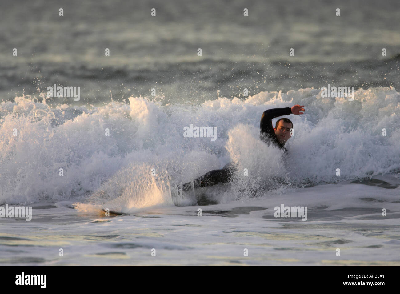 male surfer in wetsuit lying in wave having fallen off surfboard off