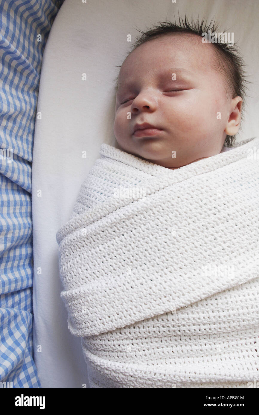 A newborn baby sleeps swaddled in a blanket in a Moses basket Stock