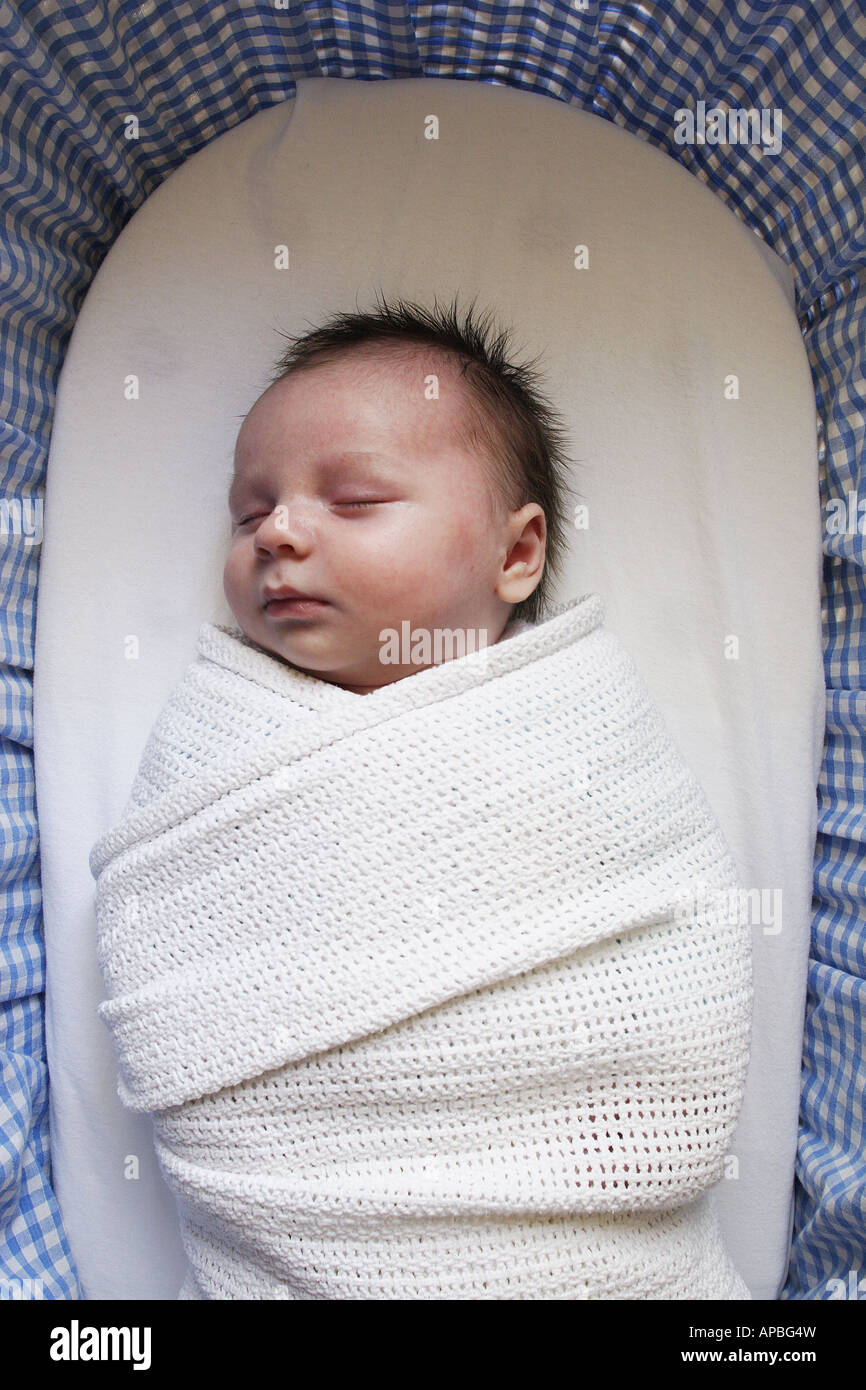 A newborn baby sleeps swaddled in a blanket in a Moses basket Stock