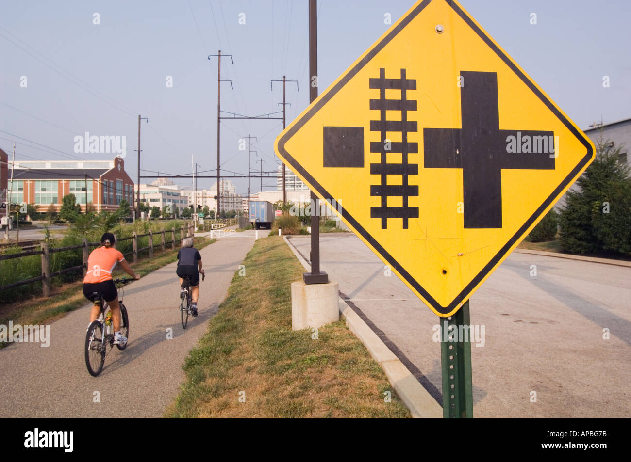 two cyclists on a rail trail riding away with a sign warning or railroad track hazard in foreground in Conshohocken Pennsylvania Stock Photo