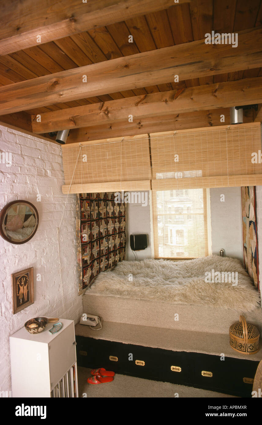 Split cane divider blind above bed with sheepskin throw and storage drawers in sixties bedroom with beamed ceiling Stock Photo