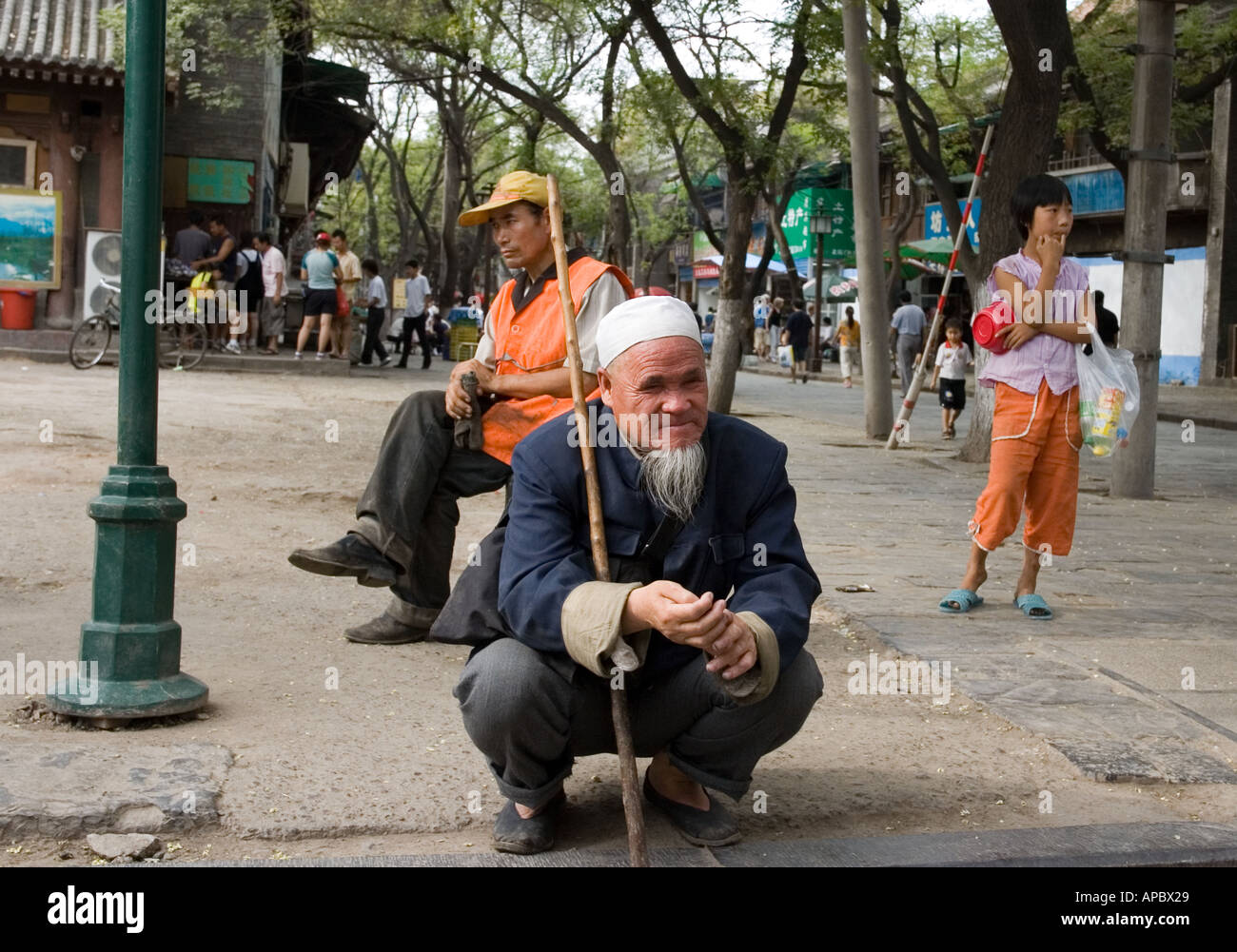 Local old man resting in squatting position in a street, Xi'an, China Stock Photo
