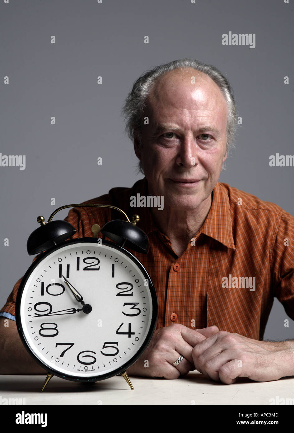 Mature man sitting at a table with an alarmclock Stock Photo