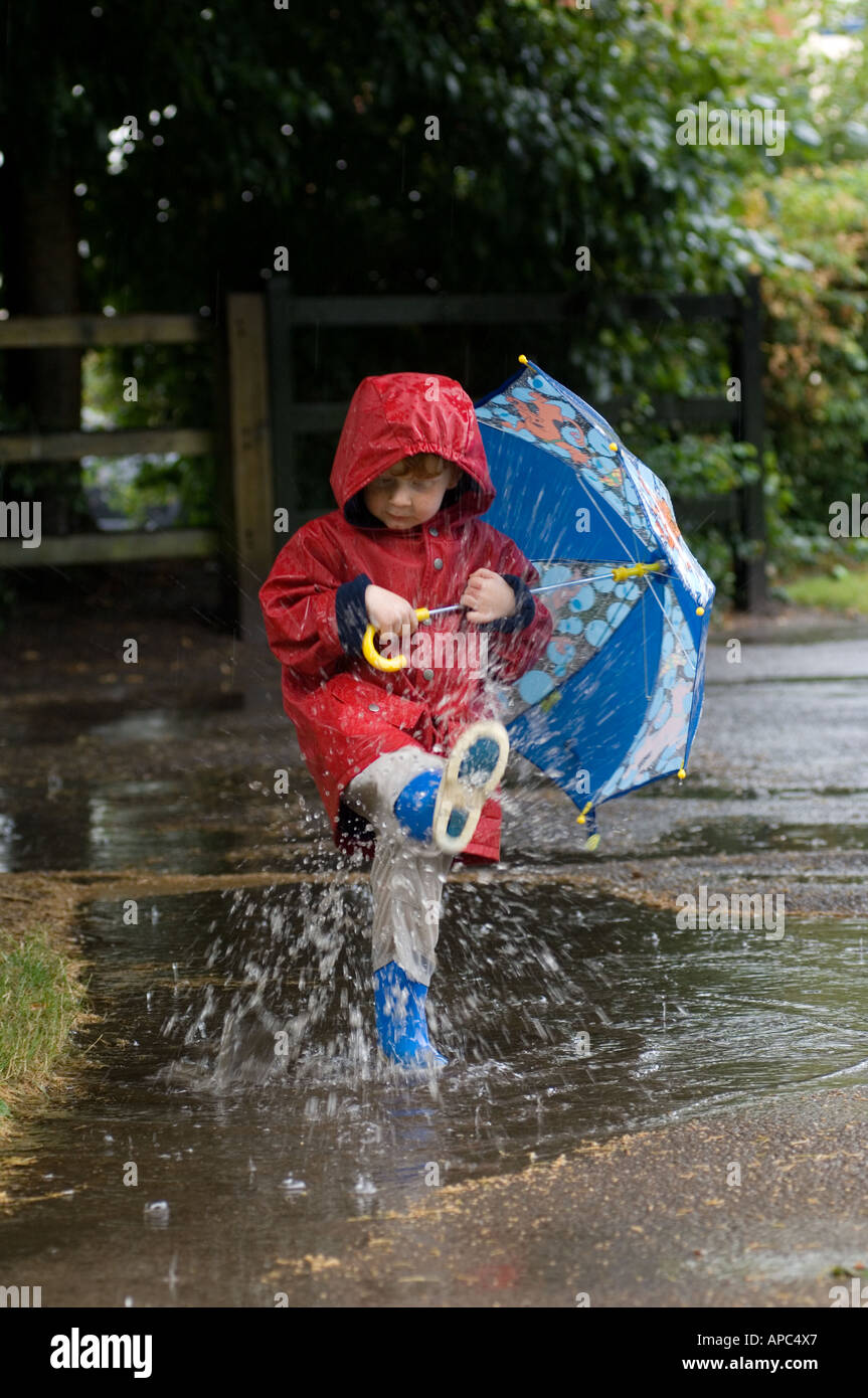 Little boy in red coat and blue umbrella splashing in the rain Stock Photo