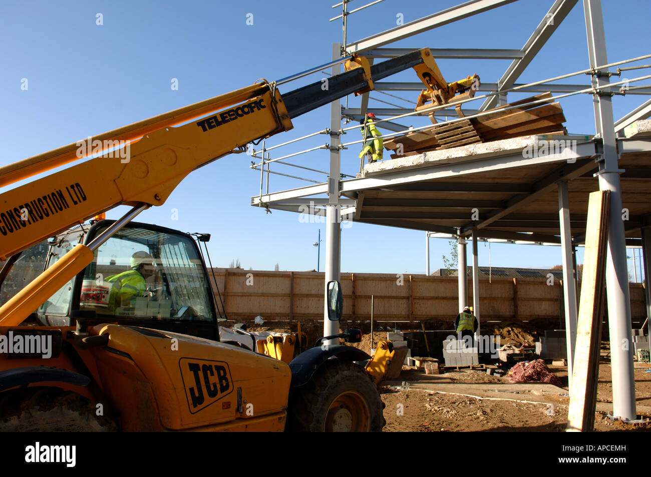 JCB fork lift lifting materials on to steel framed building Stock Photo