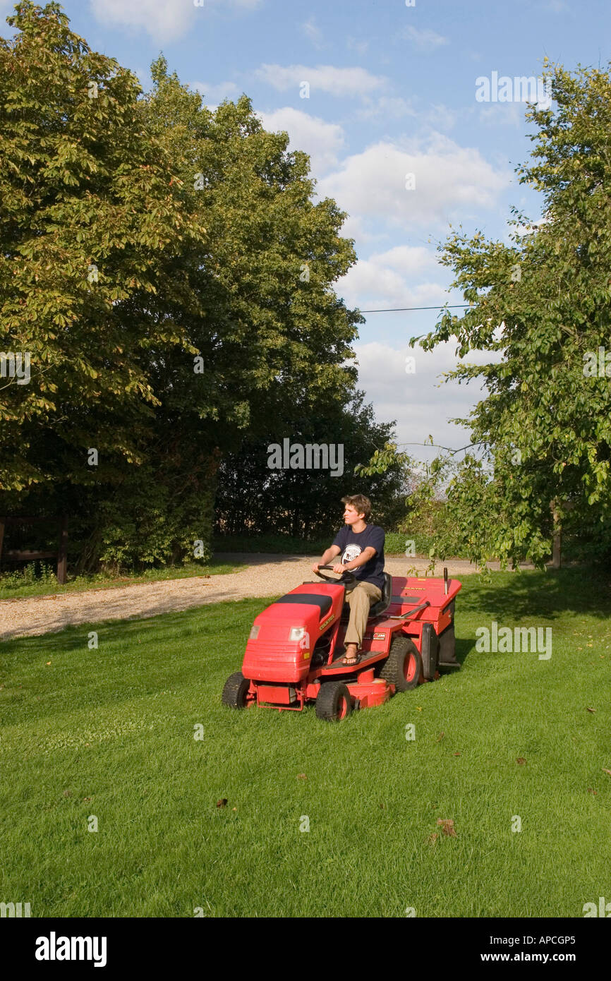 Using a ride on petrol driven tractor mower to cut garden lawn with grass collecting box Stock Photo