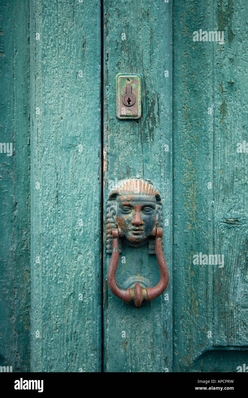 antic doorknocker in human face shape and lock on green weathered wooden door Stock Photo