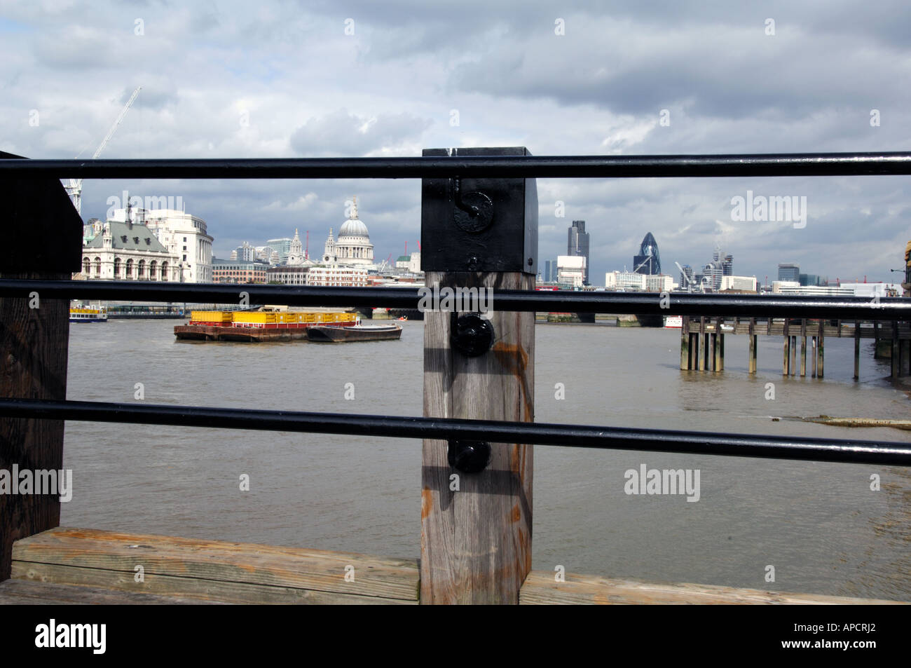 view through railing across river thames towards st pauls cathedral with pavement and bollard in foreground south bank london uk Stock Photo