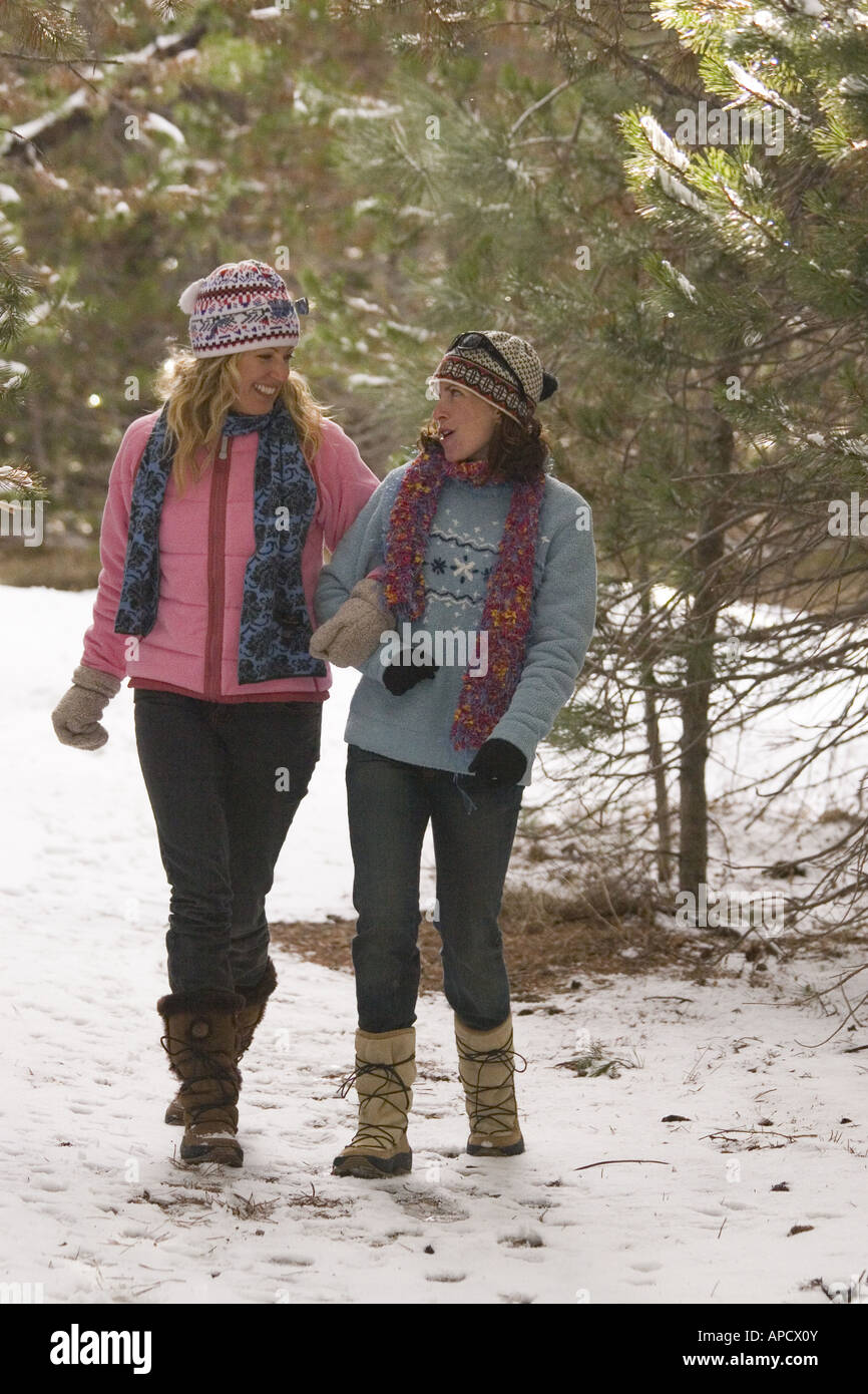 Two women friends taking a walk through the woods on a snowy day near ...