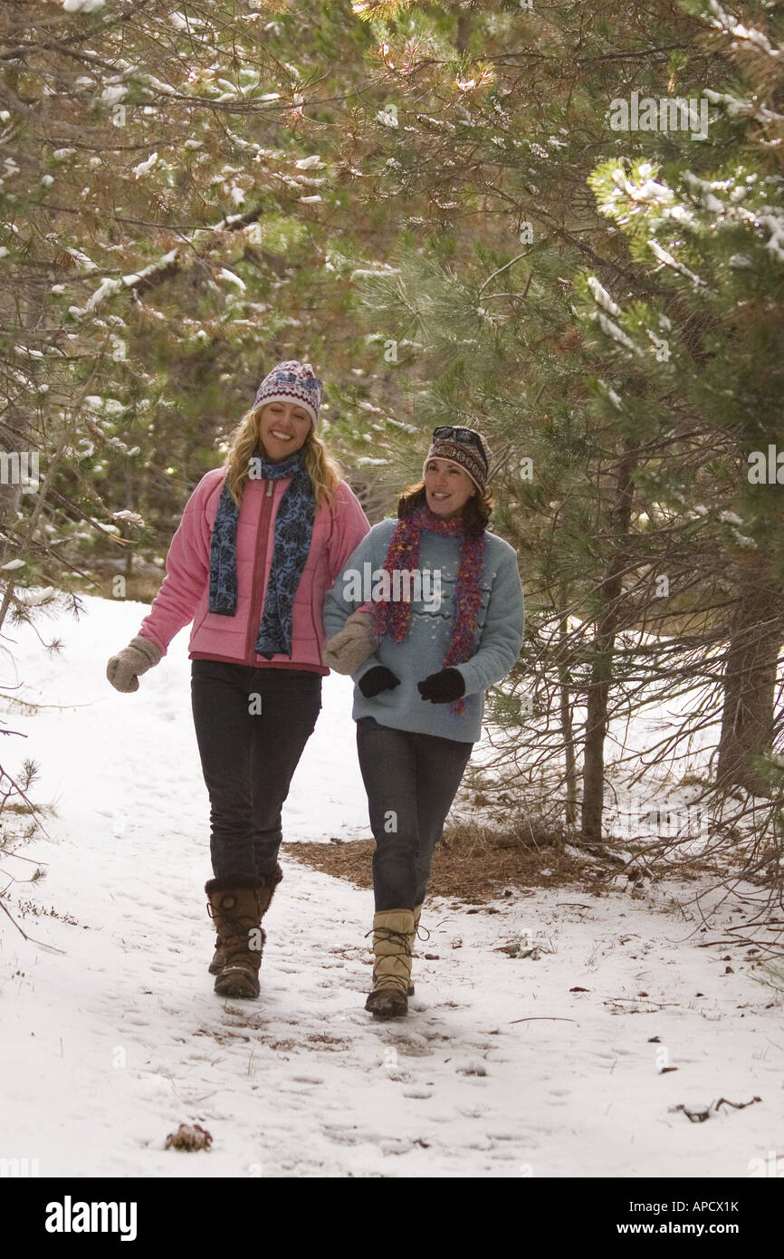 Two women friends taking a walk through the woods on a snowy day near ...