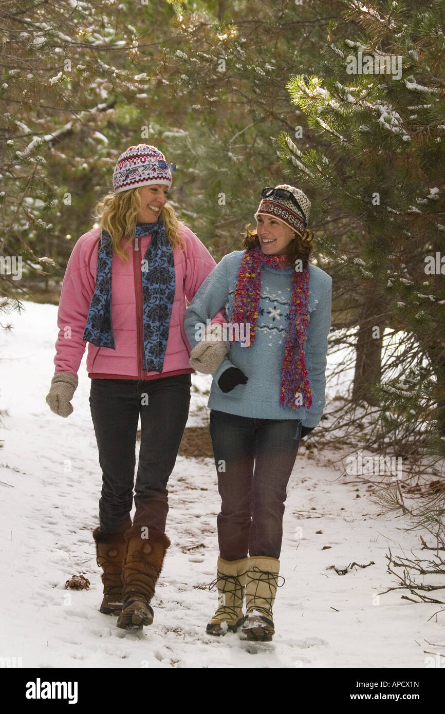 Two women friends taking a walk through the woods on a snowy day near ...