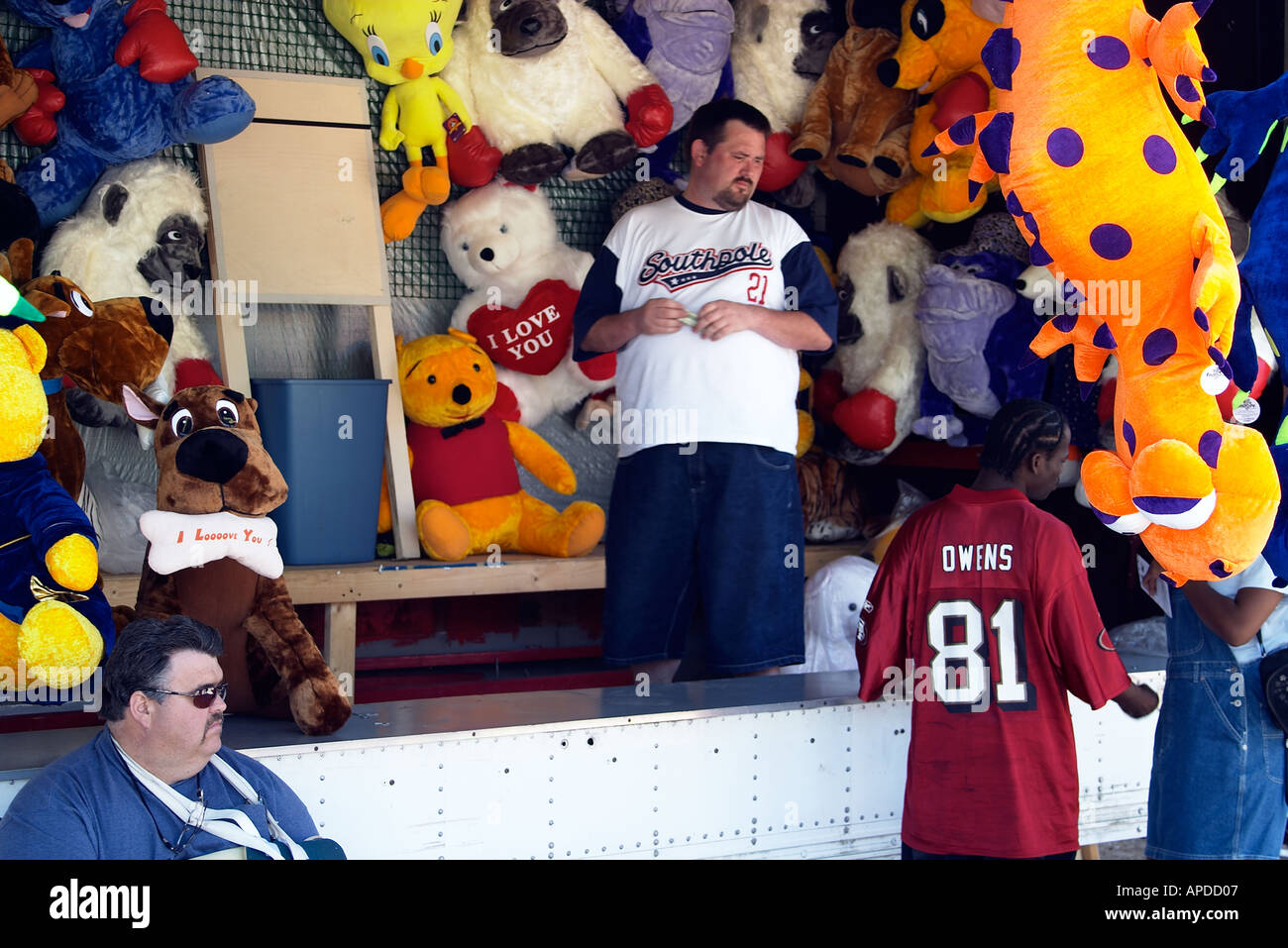 A carnival vendor surrounded by stuffed animals talks to customers