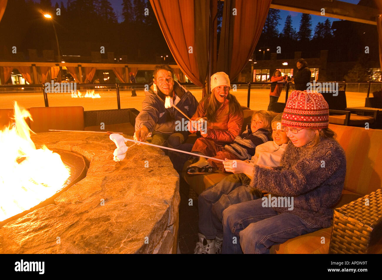A family sits around a fire roasting marshmallows by an ice skating rink at Northstar ski resort near Lake Tahoe in California Stock Photo