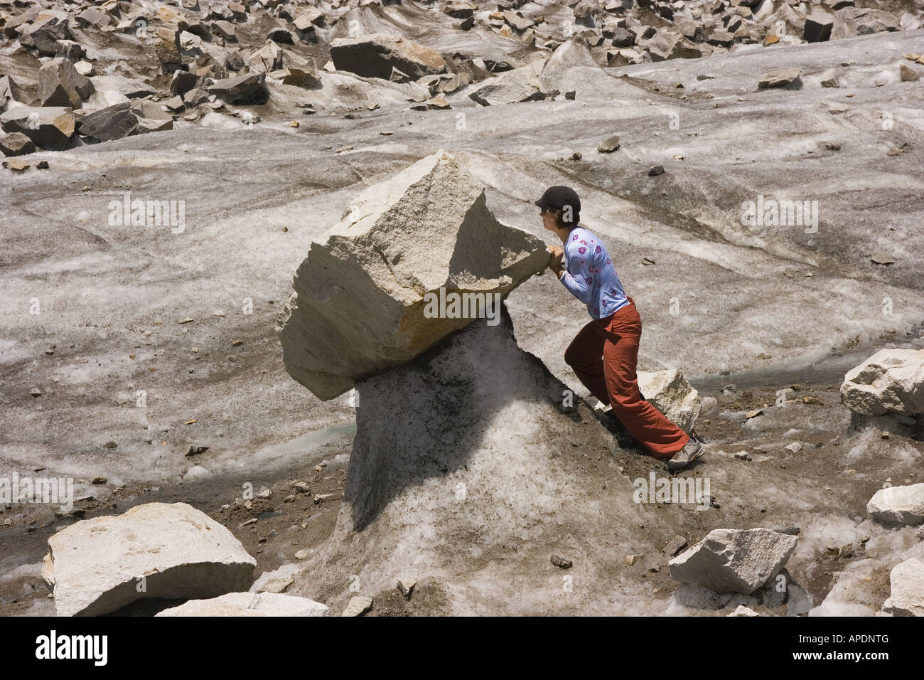 A woman pushing a rock on a glacier Stock Photo