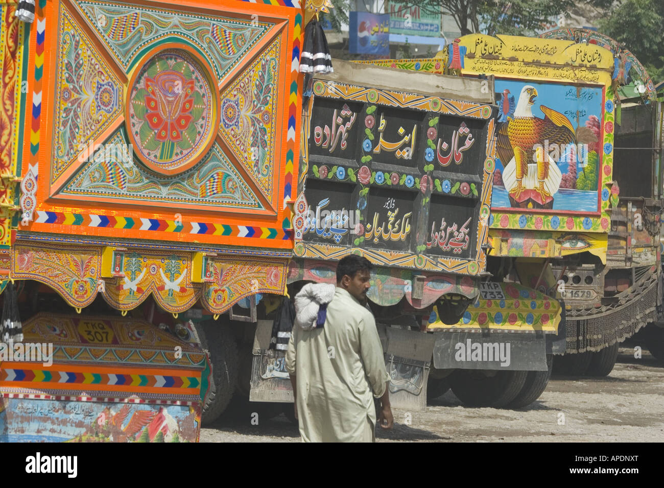 A Pakistani man walking past some colorful trucks in Islamabad in Paksitan Stock Photo