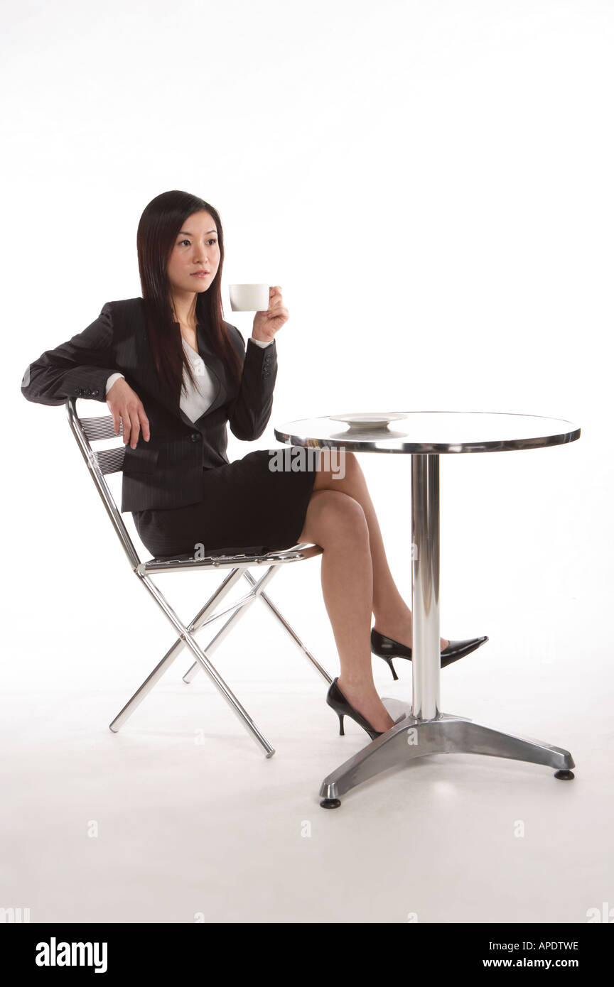 Young woman in business suit relaxing on chair and holding a cup full length Stock Photo