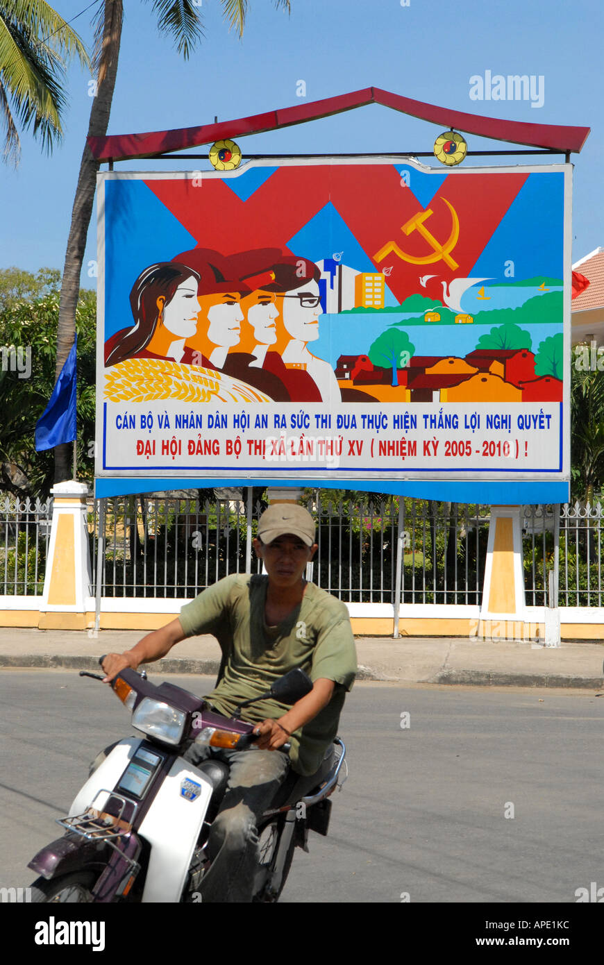 Motorbike passing in front of a socialist poster in the city of Hoi An Vietnam Stock Photo