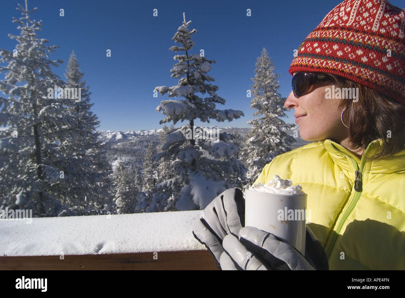 Stock photo a woman drinking hot chocolate on the deck of a ski lodge…