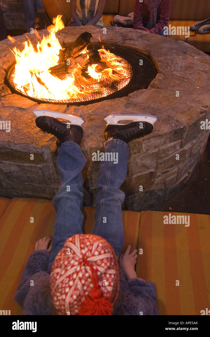 A child in ice skates sitting by a fire at Northstar ski resort near Lake Tahoe, California Stock Photo
