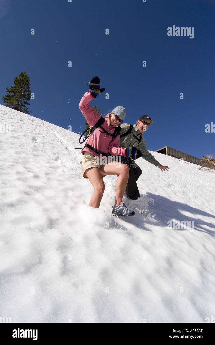 A smiling woman and man running and sliding through spring snow on Donner Summit in the Sierra mountains of California Stock Photo