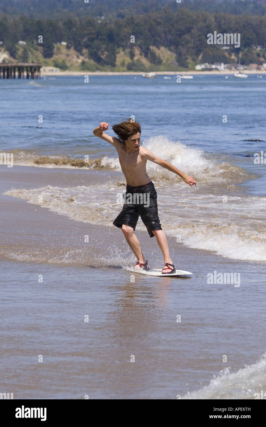 A young boy skim boarding on the beach on the Pacific Ocean in Santa