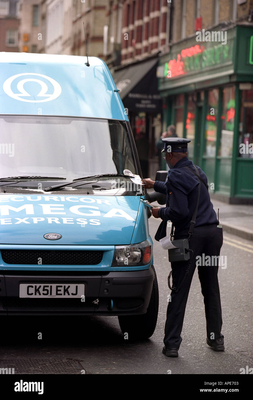 A traffic warden issues a parking ticket to a delivery van in Soho London England UK Stock Photo