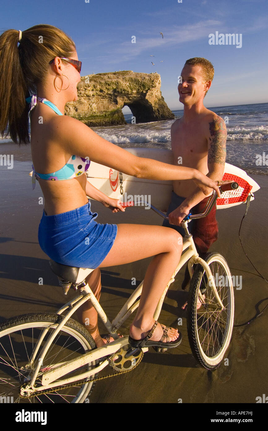 A woman on a cruiser bike and a man with a surfboard on the beach at Natural Bridges State Park in Santa Cruz in California Stock Photo