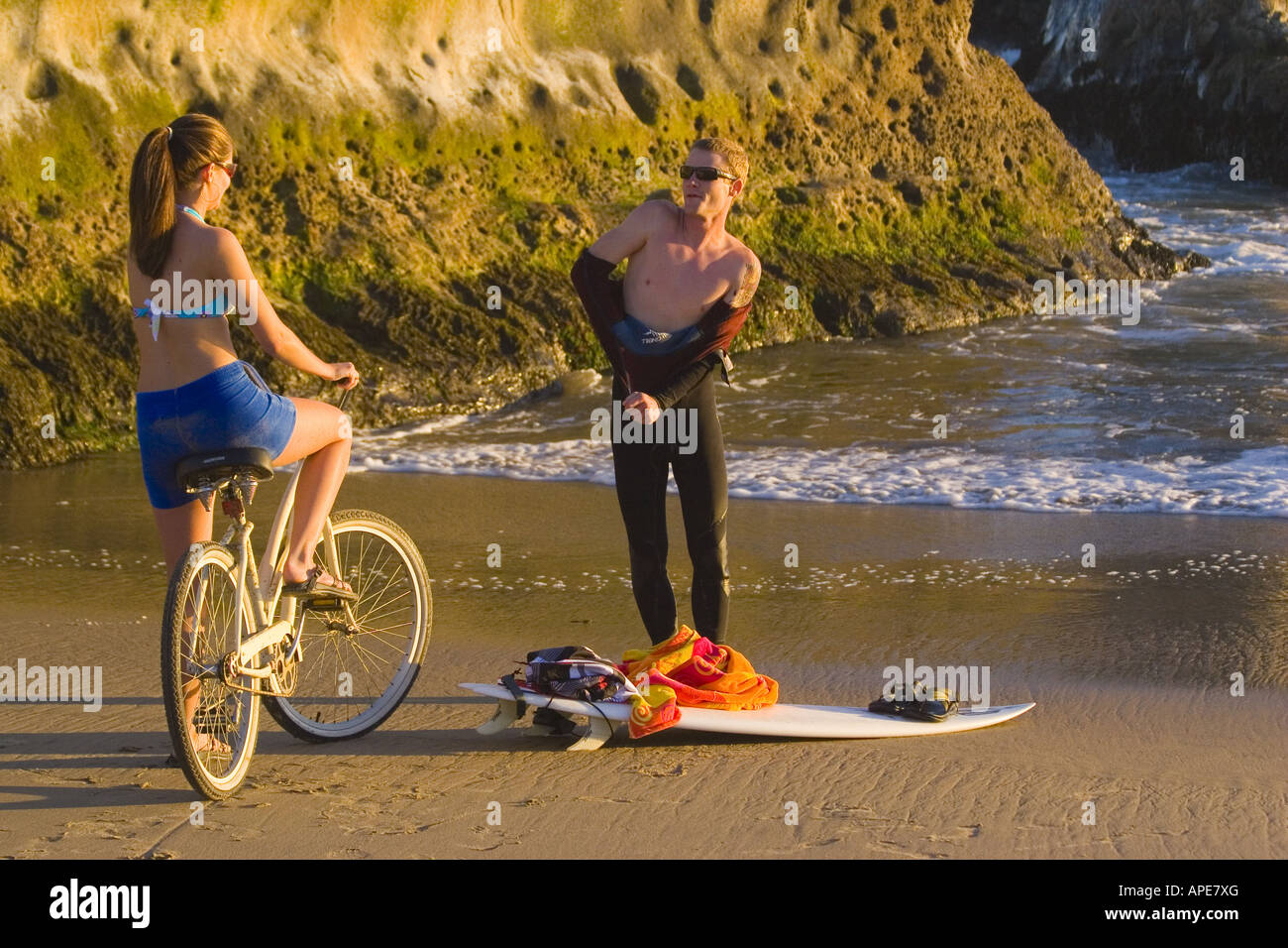 A woman on a cruiser bike and a man with a surfboard on the beach at Natural Bridges State Park in Santa Cruz in California Stock Photo