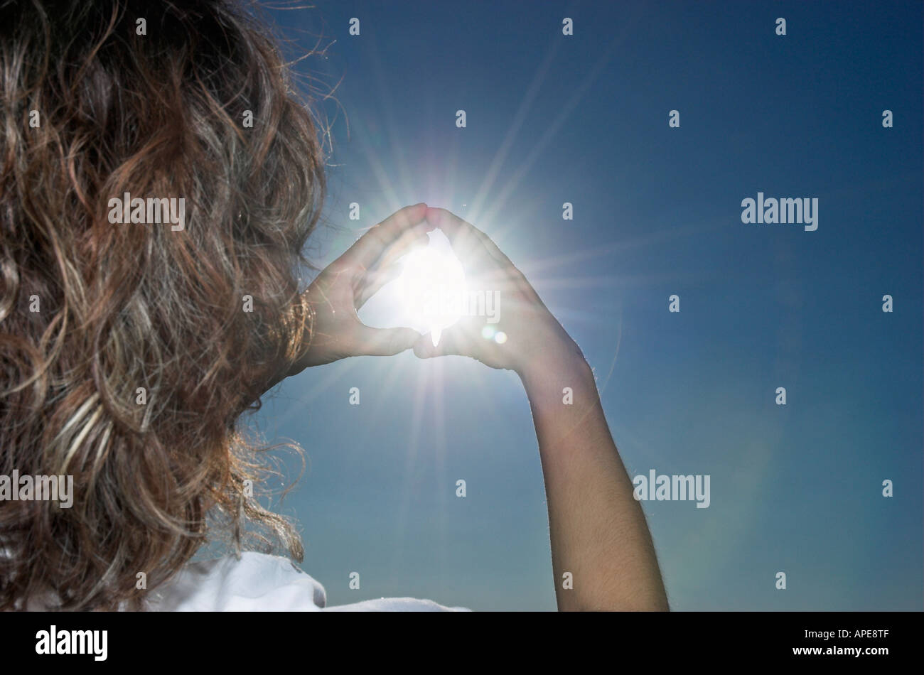 Young woman raising hands to sky framing sun, rear view Stock Photo - Alamy