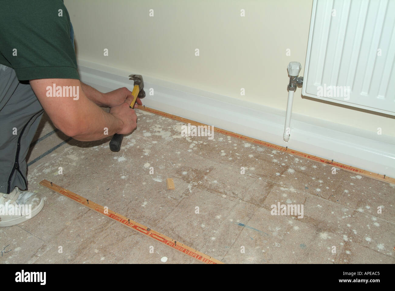 Carpet fitter at work fitting gripper strips against skirting boards around perimeter onto bedroom chipboard flooring Stock Photo