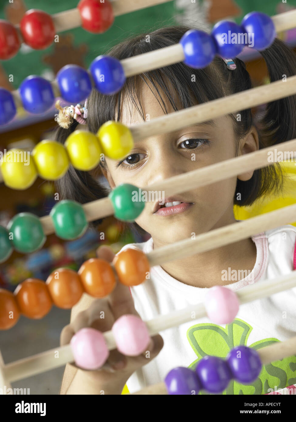 South Asian Indian girl sitting in front of abacus and calculating beads sliding on wires in nursery school MR Stock Photo