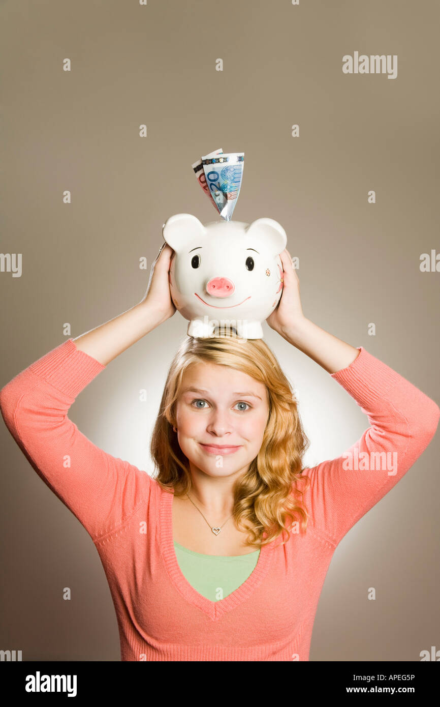 Teenage girl holding piggy bank on head Stock Photo - Alamy