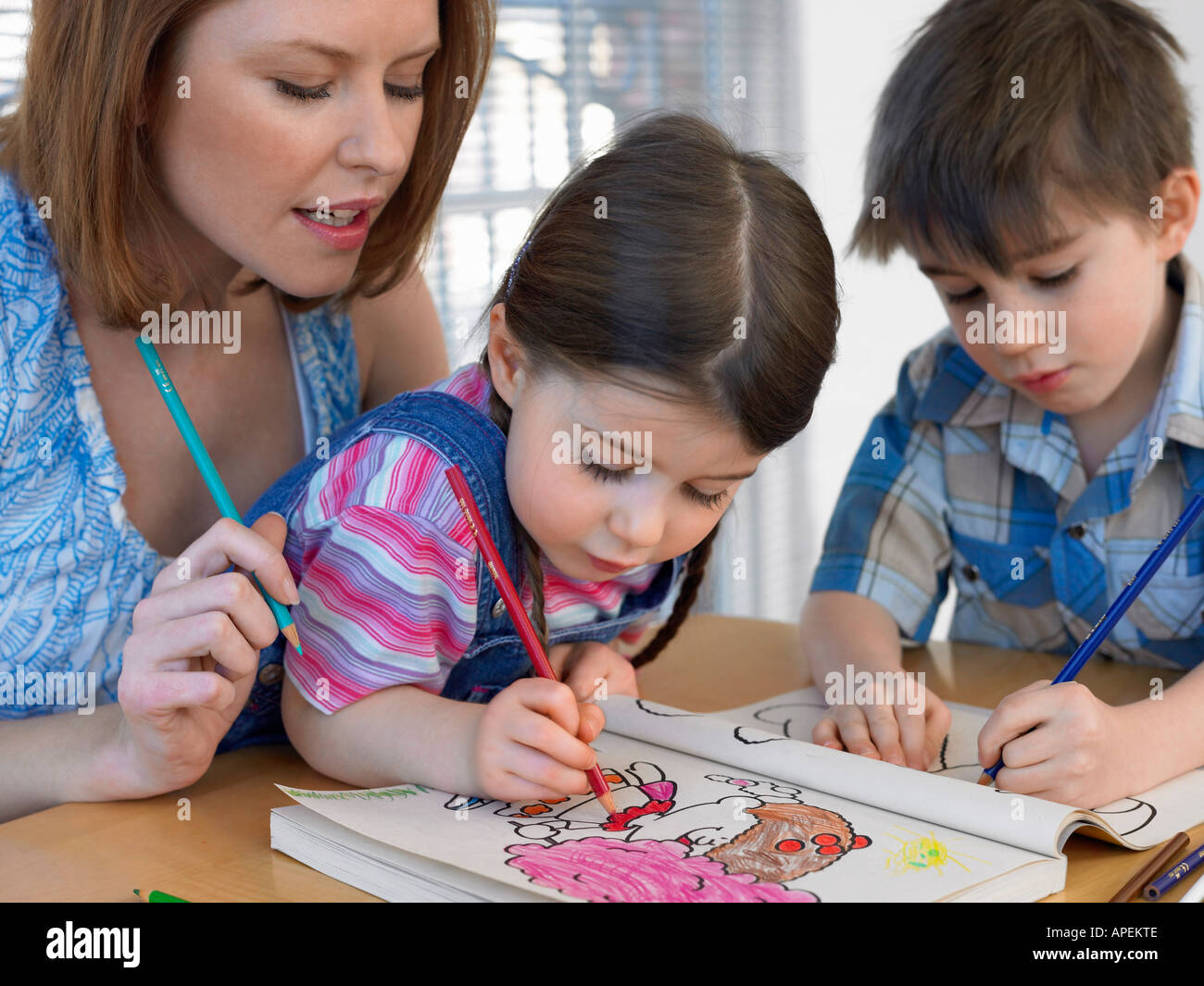 Mother and children (3-6) colouring in book, at home Stock Photo
