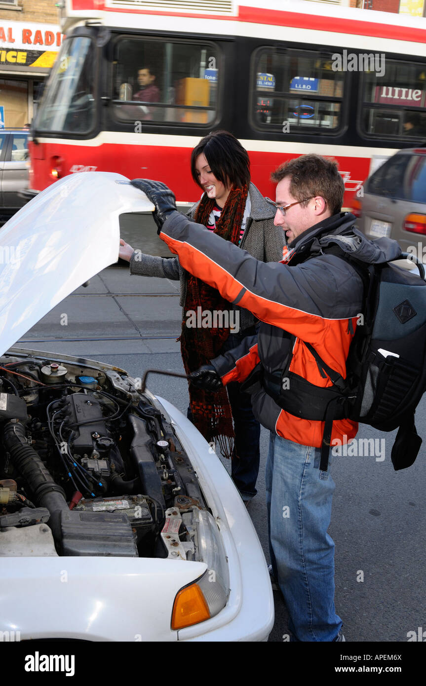 Man helping woman with broken down car by the side of the road while the TTC Queen streetcar passes by Toronto Stock Photo