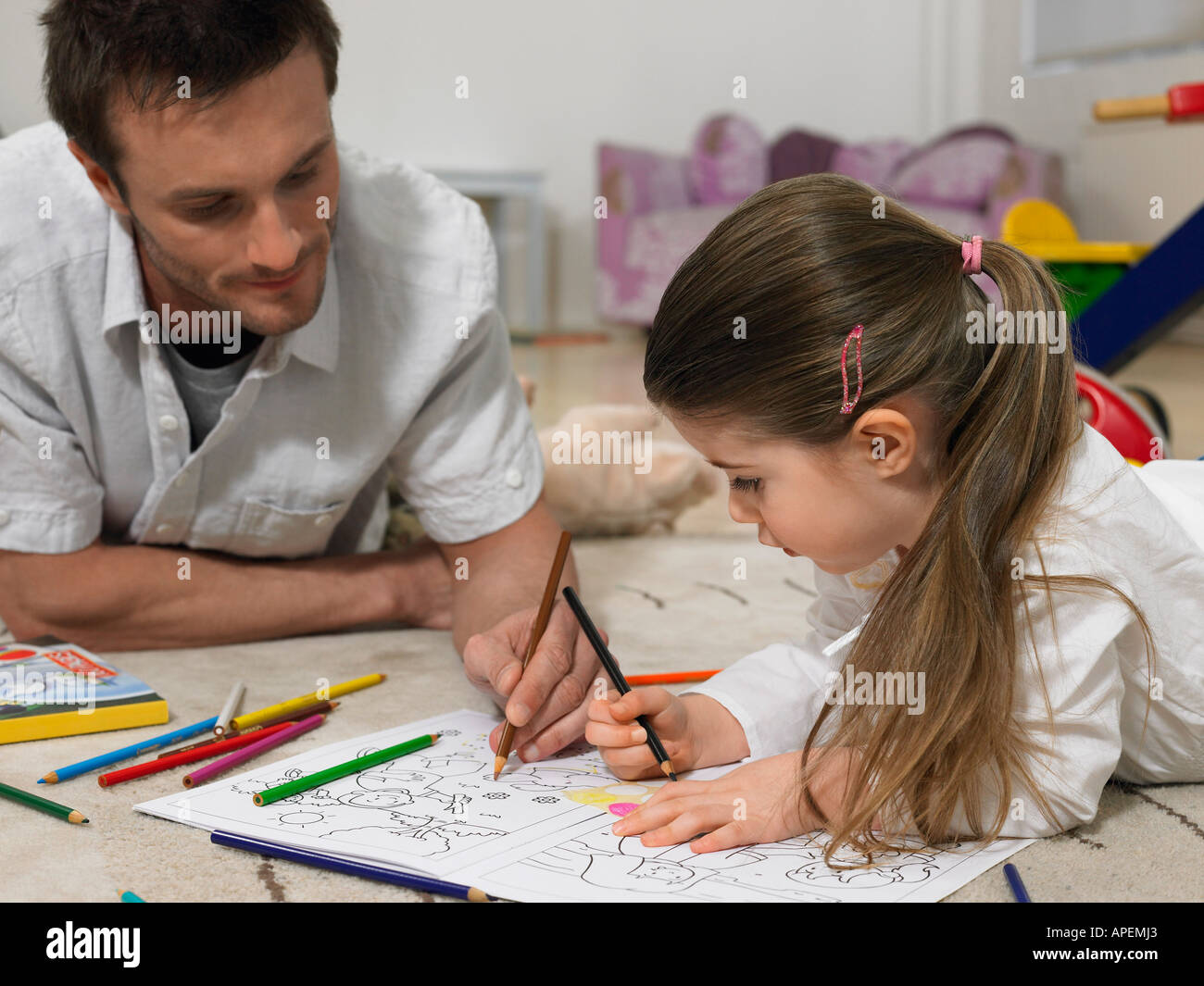 Father and daughter (3-4) colouring in book on floor Stock Photo