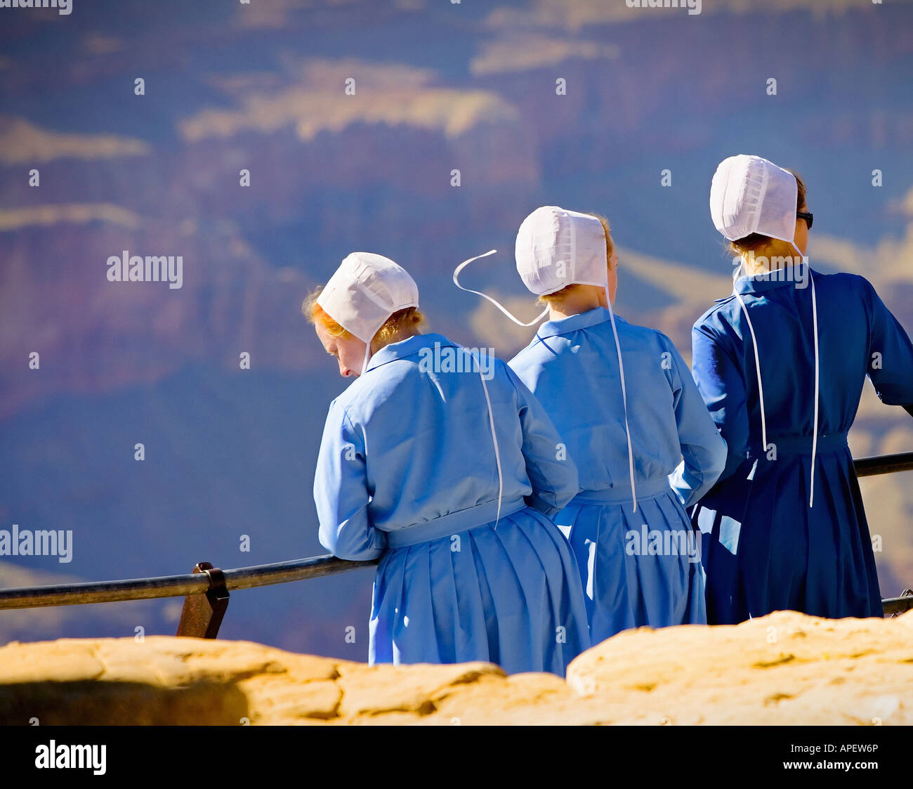 Amish girls in traditional blue dress and white hats overlooking the Grand Canyon on ledge with metal banister. (1) Stock Photo