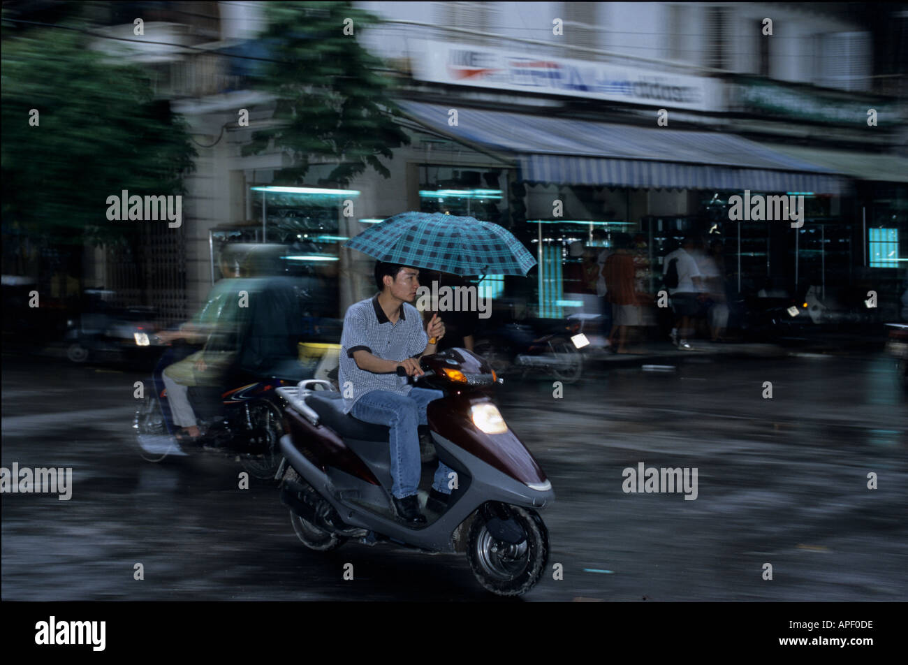 Young man on motorcycle scooter with umbrella in rain Hanoi Vietnam Stock Photo