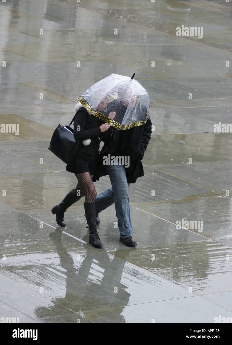 Young couple under umbrella walking swiftly to escape the rain Stock Photo